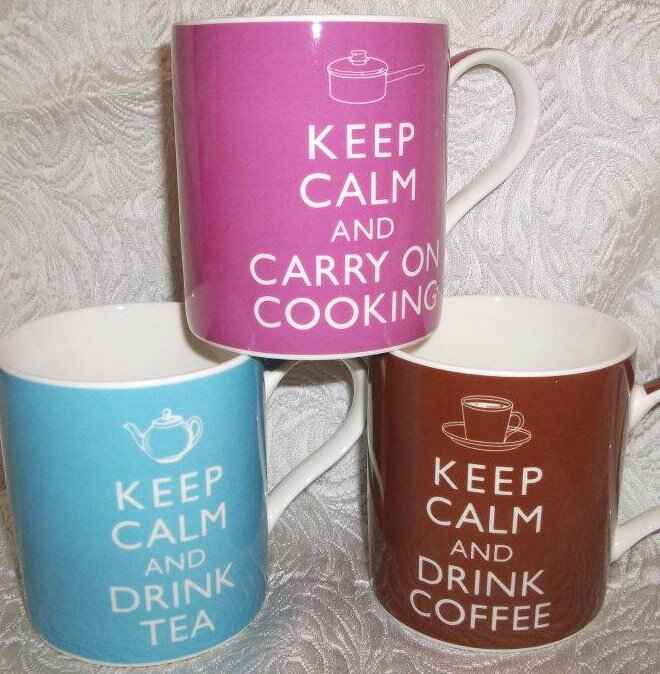 Three mugs with “Keep Calm and...” mugs stacked. A pink one says “Keep Calm and Carry on Cooking”. A light blue says “Keep Calm and Drink Tea”. A brown one says “Keep Calm and Drink Coffee. Photo